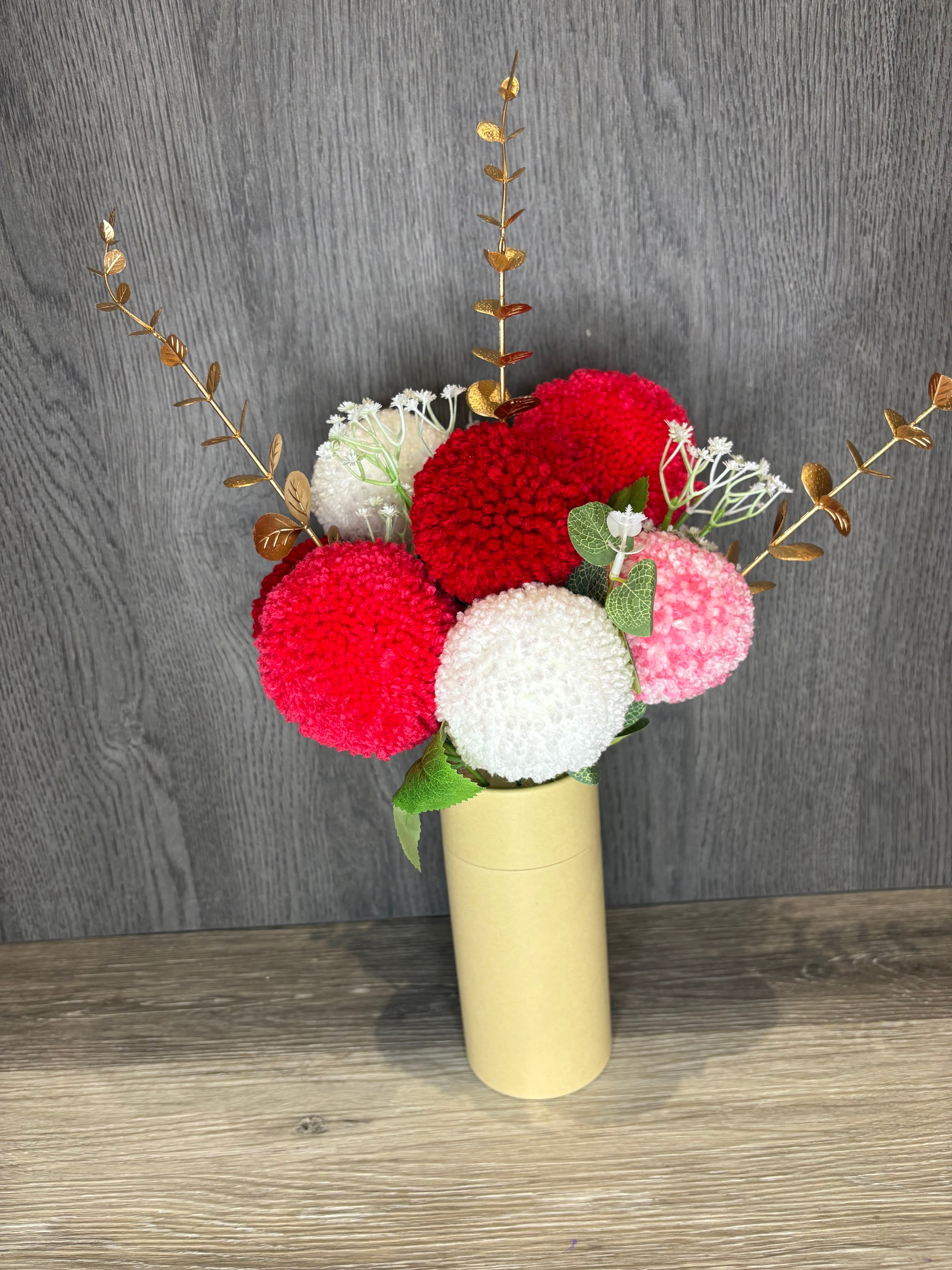Decorative pom-pom flowers in red, white, and pink on a wooden surface.